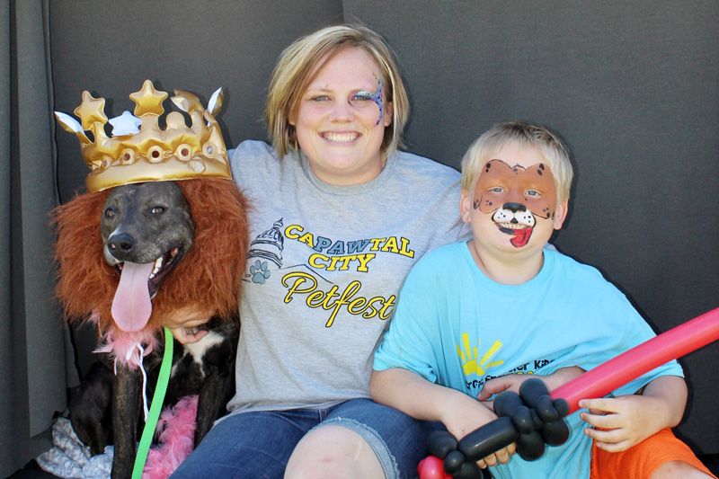 a woman and a child wearing face paint pose with a dog dressed in a crown