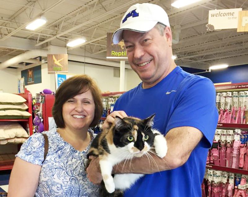 A man and woman pose with a cat