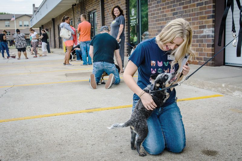 a woman kneels to pet an excited puppy