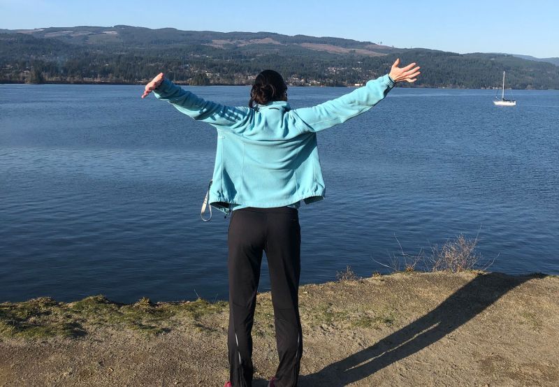 a woman with arms up facing a body of water