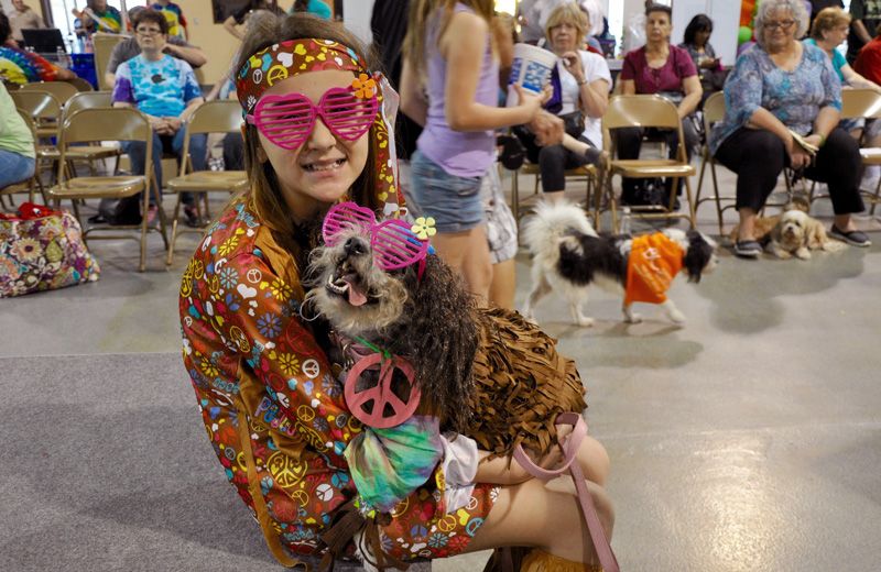 A girl holds a dog, both dressed as hippies