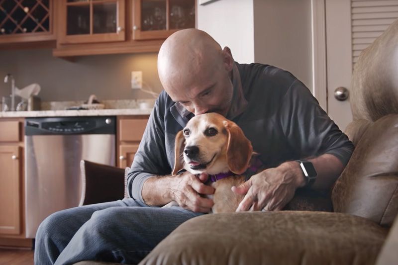 a man leans down to kiss his dog's head