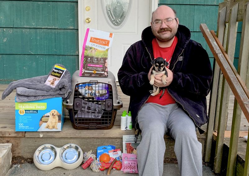 a man holds his puppy while surrounded by pet supplies on his porch