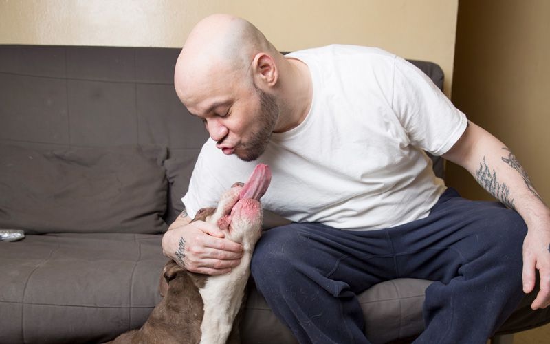 a man leans down to get a kiss from his dog