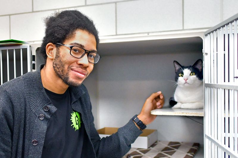 a man posing with a cat in a shelter kennel