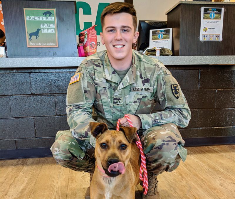 a man in military uniform poses with his shelter dog