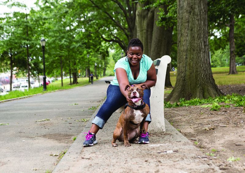 a woman sitting on a park bench pets a dog
