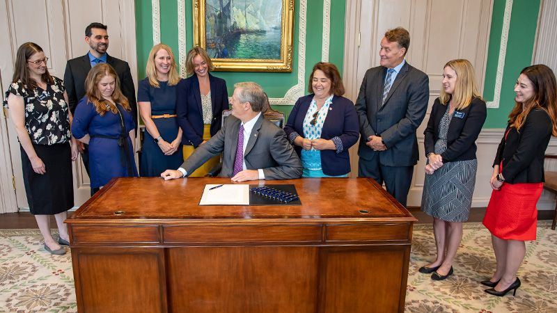 People standing around MA Governor Charlie Baker's desk for a bill signing event. 