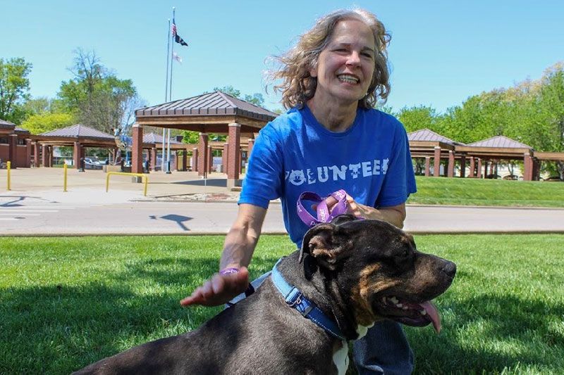 a kneeling woman smiles as she pets a large dog