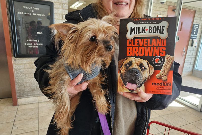 a woman holds up a small dog and box of dog treats