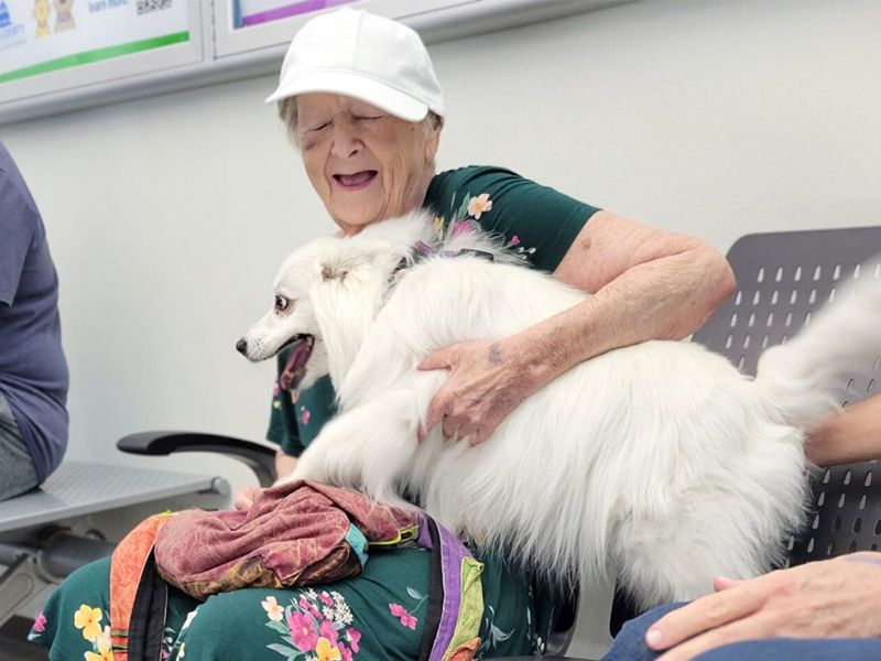 an older woman smiles as she clutches her dog