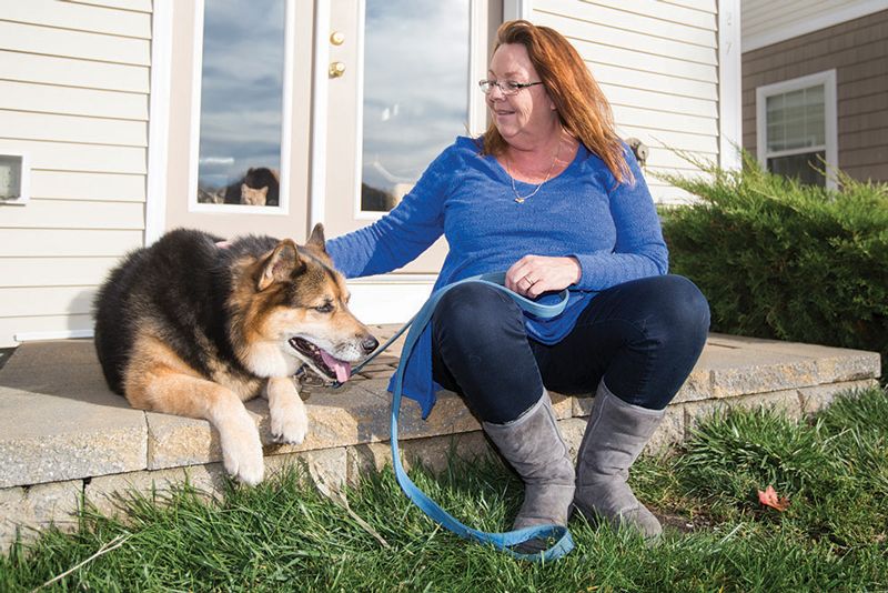 a woman pets her dog while they both sit on a porch