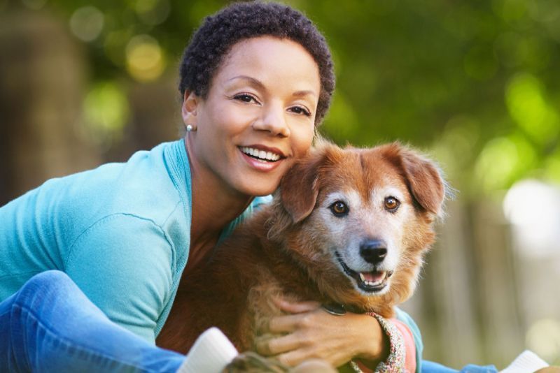 a woman leaning forward to hug her senior dog