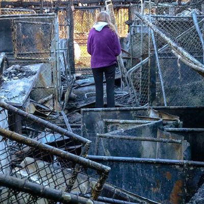 a woman stands amidst the debris of a burned shelter