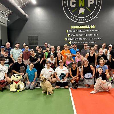 a large group of people pose with a dog on a pickleball court