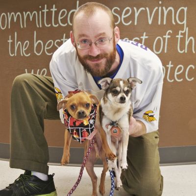 a man kneels and holds up two small dogs