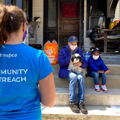 a shelter worker approaches a parent, child and their dog sitting on their porch
