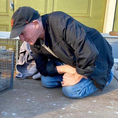 a man kneels in front of a cat in a humane trap