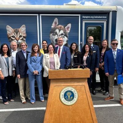 a group of people gathered around a podium standing in front of an animal shelter transfer vehicle