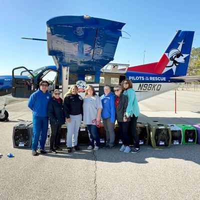 a group of people posing next to a plane with pet carriers