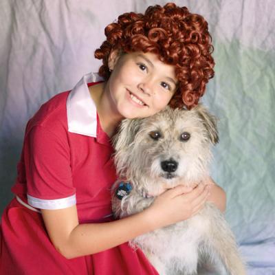 a girl dressed as Annie hugging a dog