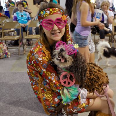 A girl holds a dog, both dressed as hippies