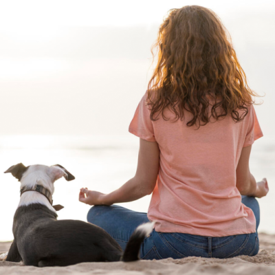 a woman meditating on a beach beside her dog