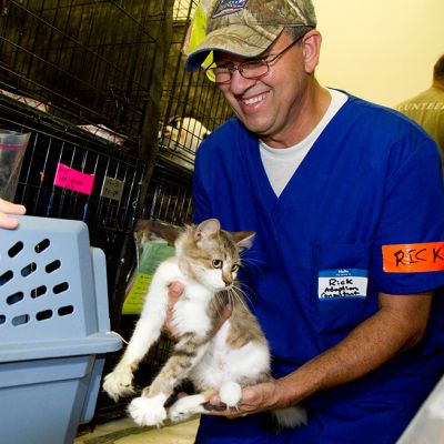 A man smiles as he transfers a small cat into a carrier