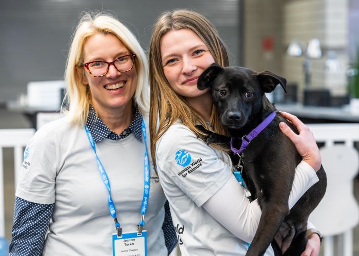 Two volunteers holding a black dog