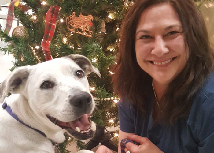 a smiling woman poses next to a white dog in front of a Christmas tree
