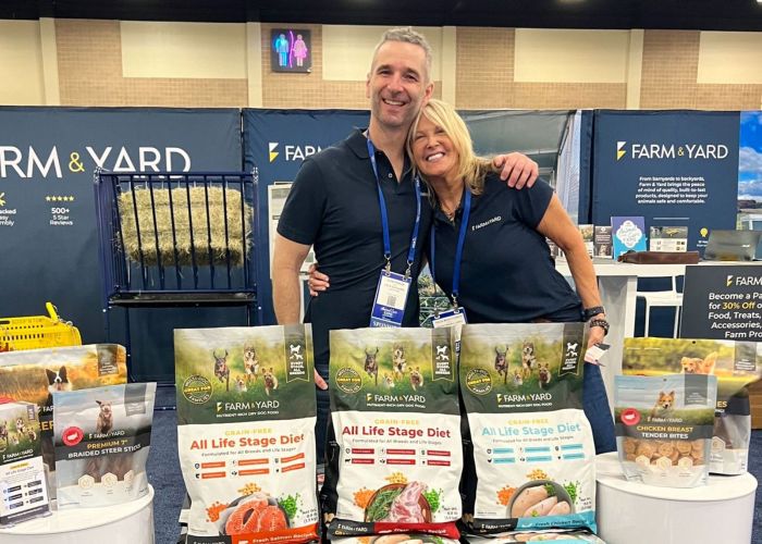 a man and a woman pose surrounded by pet food and brochures