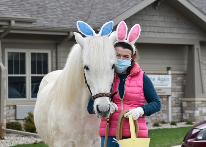 a woman poses next to a white horse, both wearing bunny ears