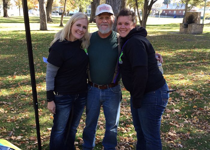 two women pose with an older man in a park