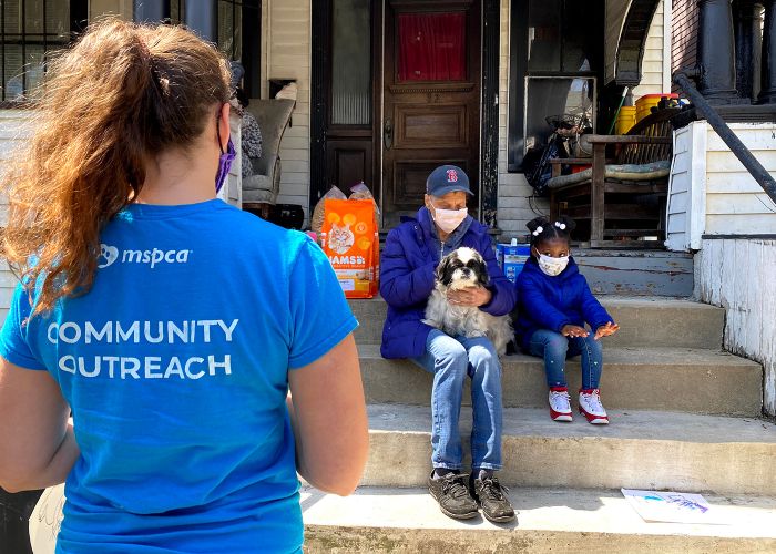 a shelter worker approaches a parent, child and their dog sitting on their porch