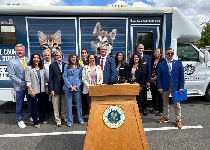 a group of people gathered around a podium standing in front of an animal shelter transfer vehicle