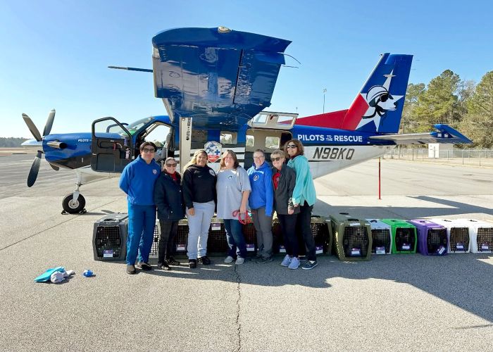 a group of people posing next to a plane with pet carriers