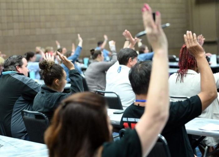 a group of people in a classroom setting all raising their hands