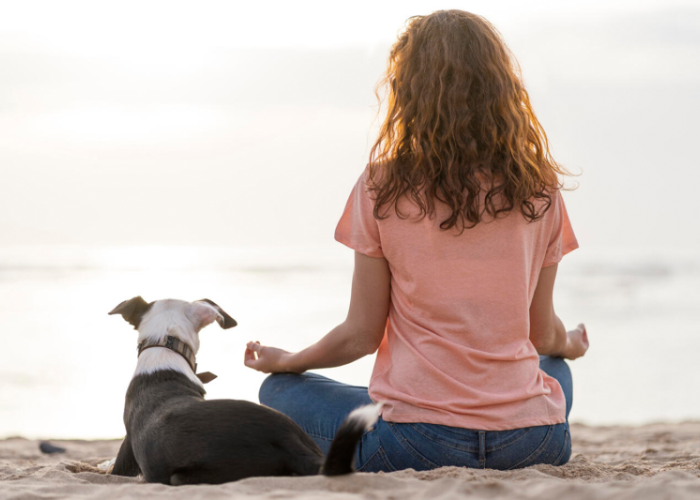 a woman meditating on a beach beside her dog