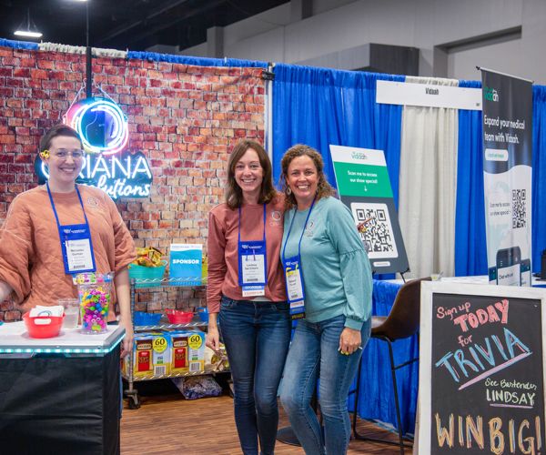 three women posing in front of an expo booth